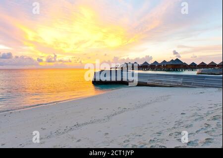 Schöner lebhafter Sonnenuntergang über dem Strand mit den Wasservillen im Indischen Ozean, Malediven Stockfoto