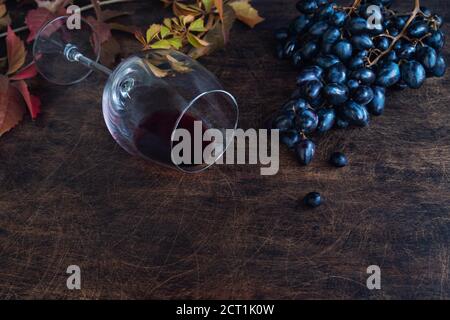Frische Bio-schwarze Trauben und ein Glas mit Rotwein auf rustikalem Sperrholzhintergrund. Leerzeichen für Text. Stockfoto