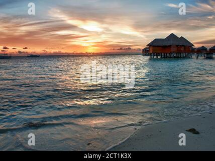 Schöner lebhafter Sonnenuntergang über dem Strand mit den Wasservillen im Indischen Ozean, Malediven Stockfoto