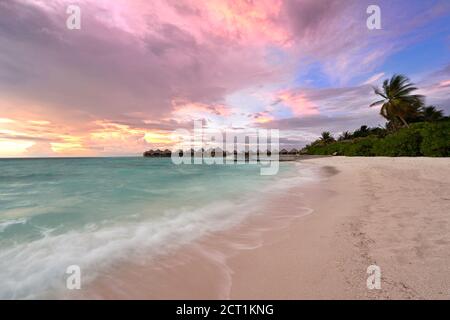 Schöner lebhafter Sonnenuntergang über dem Strand mit den Wasservillen im Indischen Ozean, Malediven Stockfoto