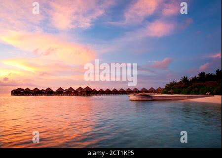Schöner lebhafter Sonnenuntergang über dem Strand mit den Wasservillen im Indischen Ozean, Malediven Stockfoto