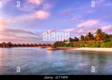 Schöner lebhafter Sonnenuntergang über dem Strand mit den Wasservillen im Indischen Ozean, Malediven Stockfoto