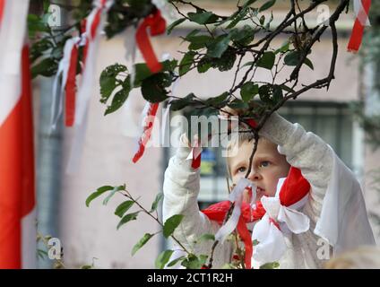 Während der Demonstration vor der Botschaft von Belarus in Kiew knüpft ein Junge ein weißes und rotes Band an einen Baumzweig.an der Kundgebung nahmen weißrussische Bürger, die in der Ukraine leben, und ukrainische Aktivisten Teil, um ihre Solidarität mit der Protestbewegung in Belarus gegen die Ergebnisse auszudrücken Die jüngsten Präsidentschaftswahlen. Stockfoto