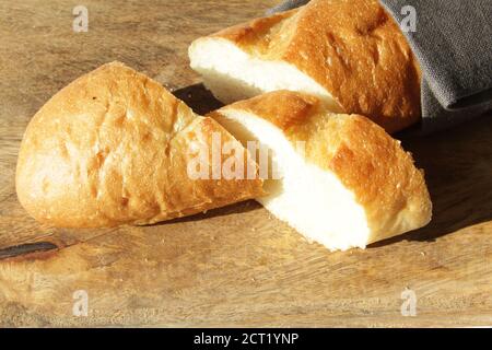 Französisches frisches weiches Brot Baguette auf einem Holzschneidebrett. Mehrere geschnittene Stücke liegen nebeneinander. Stockfoto