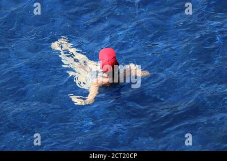 Frau in roter Mütze schwimmt im Pool, Draufsicht. Entspannung auf dem Wasser, Strandurlaub Stockfoto