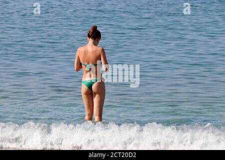 Schlanke Frau im grünen Bikini stehend in Wellen, Rückansicht. Strandurlaub, Entspannung und Freizeit am Meer Stockfoto