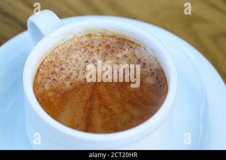 Tasse Kaffee in einer weißen Untertasse auf Holztisch, Cappuccino aus nächster Nähe Stockfoto