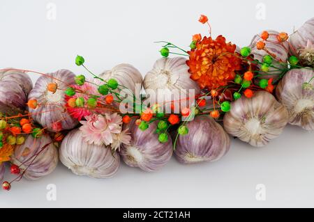 Ein mit Blumen geschmücktes Zopf aus Knoblauch vor hellem Hintergrund, aus der Nähe fotografiert Stockfoto