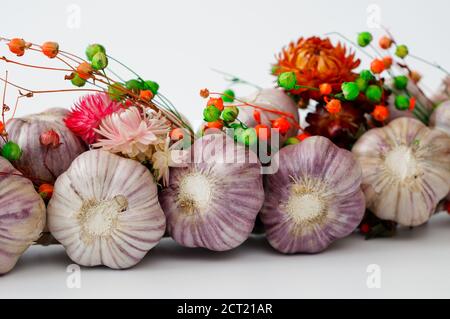 Ein mit Blumen geschmücktes Zopf aus Knoblauch vor hellem Hintergrund, aus der Nähe fotografiert Stockfoto