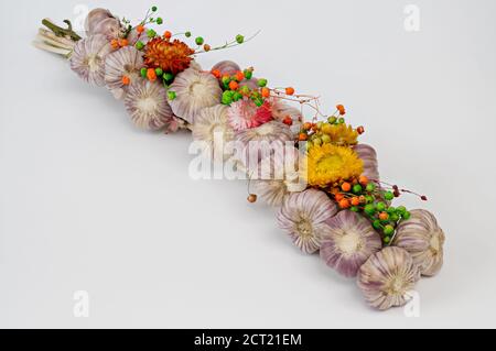 Ein mit Blumen geschmücktes Zopf aus Knoblauch vor hellem Hintergrund, aus der Nähe fotografiert Stockfoto