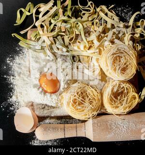 Pasta mit Zutaten - Mehl, Eier und verschiedene Werkzeuge zum Kochen auf schwarzem Tisch. Freier Platz für Text . Draufsicht. Stockfoto