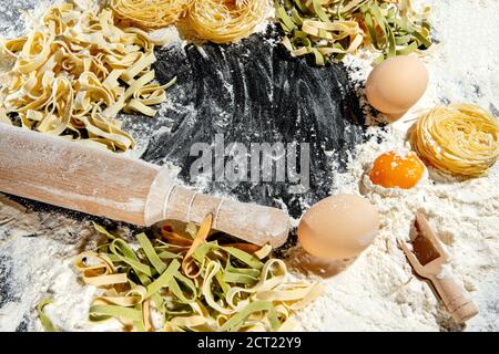 Frisch gekochte Pasta liegt auf einer dunklen, mit Mehl bestäubten Oberfläche. Italienische Pasta. Tagliatelle. Rohe Pasta. Italienische Pasta Rezept. Draufsicht, Kopierbereich Stockfoto