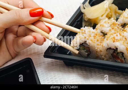 Frau essen zu Hause Sushi aus einem Behälter mit geliefert japanische Sticks Stockfoto