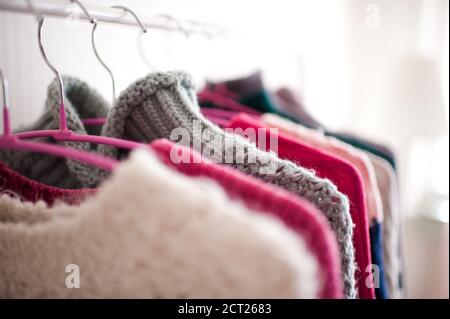 Bunte Strickkleidung hängen an Kleiderbügeln in der Nähe des Shops. Wintersaison. Selektiver Fokus. Stockfoto