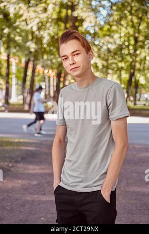 Der junge kaukasische gutaussehende Mann steht im öffentlichen Park auf dem verschwommenen Hintergrund. Stockfoto