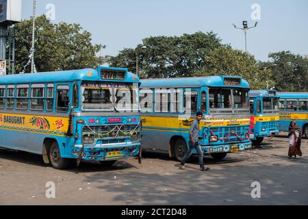 Kolkata, Indien - 1. Februar 2020: Ein nicht identifizierter Mann und eine Frau gehen an traditionellen türkisfarbenen und gelben öffentlichen Bussen vorbei, die an einer Bushaltestelle parken Stockfoto