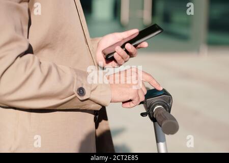 Hand des modernen Geschäftsmann in beige Trenchcoat scrolling im Smartphone Stockfoto