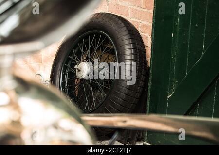 Ein Bentley 4 1/2 Liter Supercharged (The Green Hornet) Drahtrad, das sich in einer Garage des Bicester Heritage Sunday Scramble an einer Ziegelwand auflehnt. Stockfoto