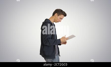Junger Mann mit digitalen Tablet beim Gehen auf Gradient Backgro Stockfoto