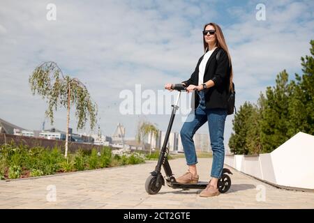 Junge Geschäftsfrau in Sonnenbrillen auf Roller im städtischen Umfeld stehen Stockfoto