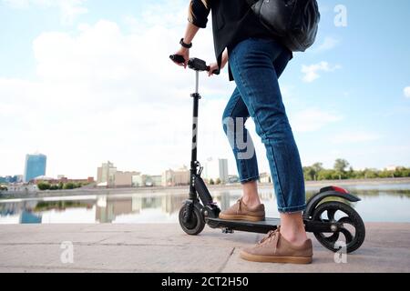 Zeitgenössische junge Frau auf Elektroroller vor stehen riverside Stockfoto