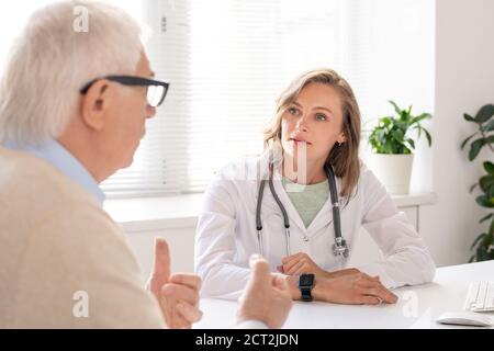 Junge blonde hübsche weibliche Arzt in Whitecoat Beratung Senior man Im Krankenhaus Stockfoto