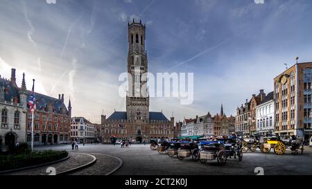 Pferdekutschen bei Sonnenaufgang auf dem Marktplatz in Brügge mit vielen historischen Gebäuden und dem berühmten Glockenturm Im Jahr 1240 Stockfoto