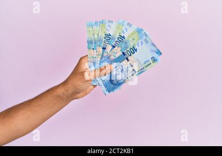 Hispanische Hand hält 100 Südafrika rands Banknoten über isolierten rosa Hintergrund. Stockfoto