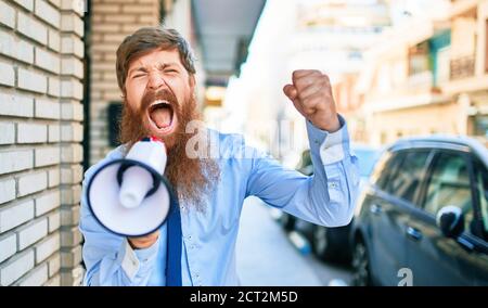 Junger rothaariger Geschäftsmann mit wütender Expression. Schreien mit Megaphon auf der Straße der Stadt. Stockfoto