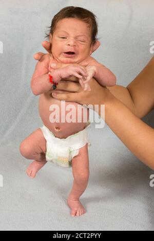 12 Tage alter neugeborener Junge, der einen Trittreflex vorführt windel trägt Glücksarmband Stockfoto