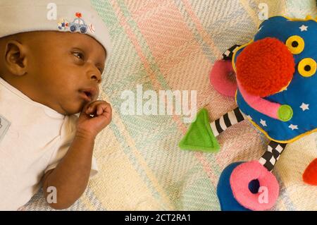 6 Wochen alt neugeborenes Baby Junge einen Monat vorzeitige Warnung Blick auf bunte Spielzeug, Tragen Mütze Stockfoto