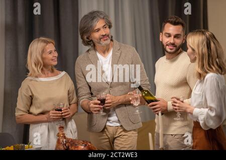 Glückliches reifes Paar mit Gläsern Wein und jungen Mann Blick auf blonde Frau Stockfoto