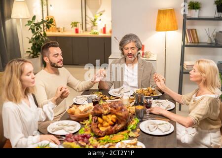 Zwei Paare in Casualwear, die die Augen geschlossen halten, während sie an der Kleidung sitzen Festlicher Tisch Stockfoto