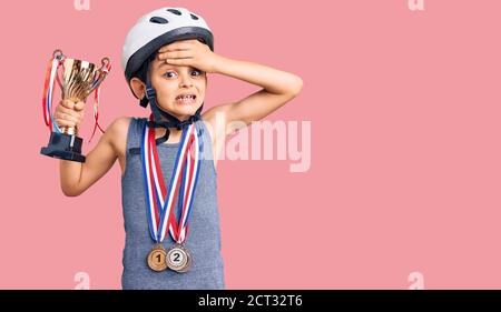 Kleine niedliche Junge Kind trägt Fahrradhelm und Siegermedaillen halten Siegertrophäe gestresst und frustriert mit Hand auf Kopf, überrascht und wütend Gesicht Stockfoto