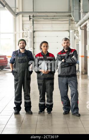 Drei erfolgreiche interkulturelle Arbeiter des modernen Kfz-Wartungszentrums Stockfoto