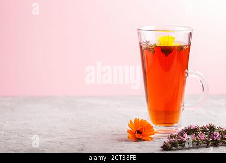 Glas Kräutertee mit Ringelblume und Ysop auf grauem und rosa Hintergrund. Morninig, Frühling, gesundes Getränkekonzept. Seitenansicht, selektiver Fokus, Kopieren Stockfoto
