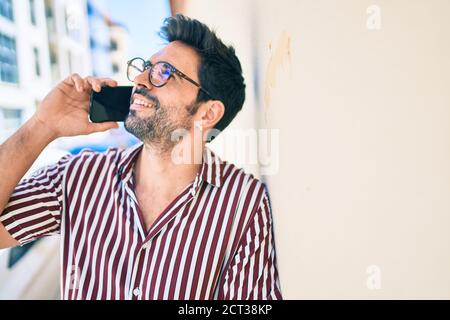 Junge gutaussehende hispanischen Mann mit Bart lächeln glücklich im Freien sprechen Am Telefon Stockfoto