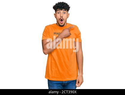 Junger arabischer Mann trägt T-Shirt mit Glück Wort Nachricht überrascht zeigt mit Finger zur Seite, offenen Mund erstaunt Ausdruck. Stockfoto