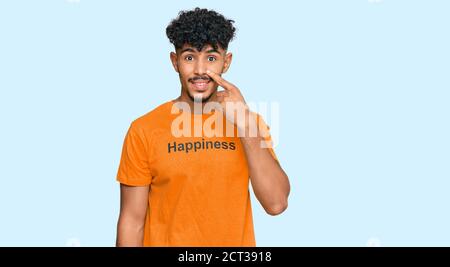 Junger arabischer Mann trägt T-Shirt mit Glück Wortmeldung zeigt mit der Hand Finger auf Gesicht und Nase, lächelnd fröhlich. Beauty-Konzept Stockfoto