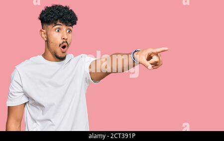 Junger arabischer Mann trägt lässiges weißes T-Shirt zeigt mit Finger überrascht voraus, offenen Mund erstaunt Ausdruck, etwas auf der Vorderseite Stockfoto