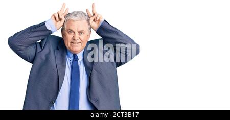 Ältere grauhaarige Mann in Business-Jacke posiert lustig und verrückt mit Fingern auf dem Kopf als Häschen Ohren, lächelnd fröhlich Stockfoto
