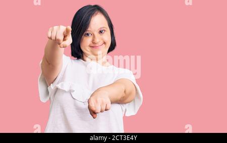 Brunette Frau mit Down-Syndrom tragen lässige weiße T-Shirt zeigt auf Sie und die Kamera mit Fingern, lächelnd positiv und fröhlich Stockfoto