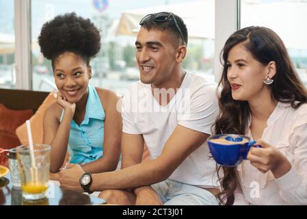 Multirassische glückliche junge Leute trinken Kaffee im Café, schwarz-weiße fröhliche Kumpels lachen Drinks genießen Spaß beim gemeinsamen Sitzen am Restauranttisch, verschiedene Freunde teilen sich das Mittagessen beim Treffen. Stockfoto
