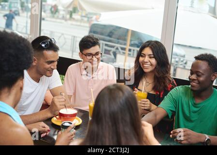 Multirassische glückliche junge Leute trinken Kaffee im Café, schwarz-weiße fröhliche Kumpels lachen Drinks genießen Spaß beim gemeinsamen Sitzen am Restauranttisch, verschiedene Freunde teilen sich das Mittagessen beim Treffen. Stockfoto