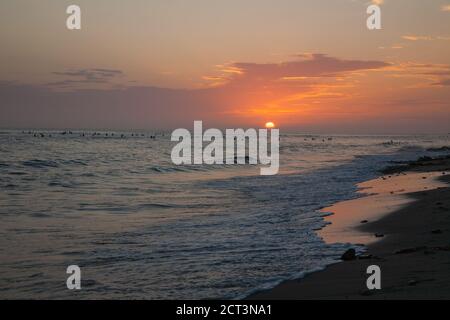 Surfer in der Ferne warten auf die perfekte Welle bei Sonnenuntergang am San Onofre Beach, Kalifornien Stockfoto