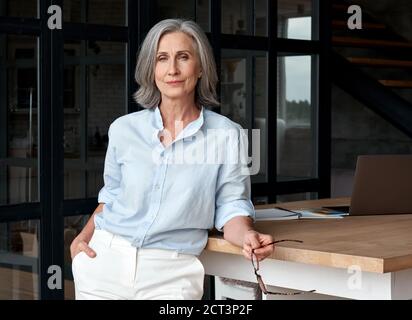 Selbstbewusst stilvolle Frau mittleren Alters am Büroarbeitsplatz, Porträt. Stockfoto