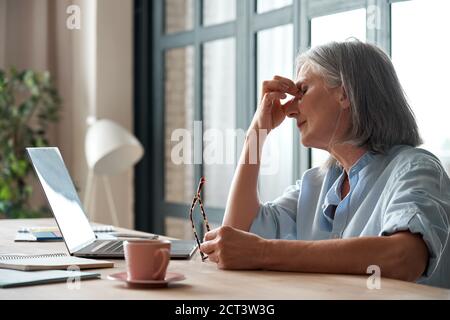 Müde alte Geschäftsfrau zieht aus Brille Gefühl Augenbelastung aus dem Computer. Stockfoto