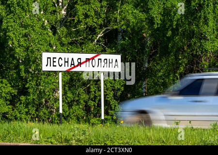 Straßenschild Ende der Stadt Lesnaya Polyana oder Lesnaya Polyana, Satellitenstadt Kemerowo, grüner Wald, Gras und graues Auto verschwommen durch den Verkehr Stockfoto