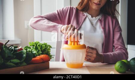 Rothaarige Frau quetscht Saft aus Obst und Gemüse an Zuhause während Diät und Schlankheitskur Stockfoto