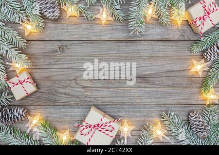 Alte Holzbretter mit Tannenzweigen, weihnachtsgeschenken und leuchtender Sternengirlande verziert Stockfoto